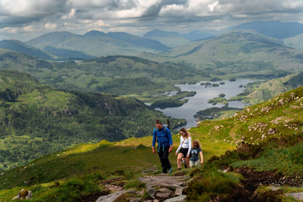 Group of two women and one man hiking mountain Torc. In background is Killarney national park and Upper Lake. Killarney