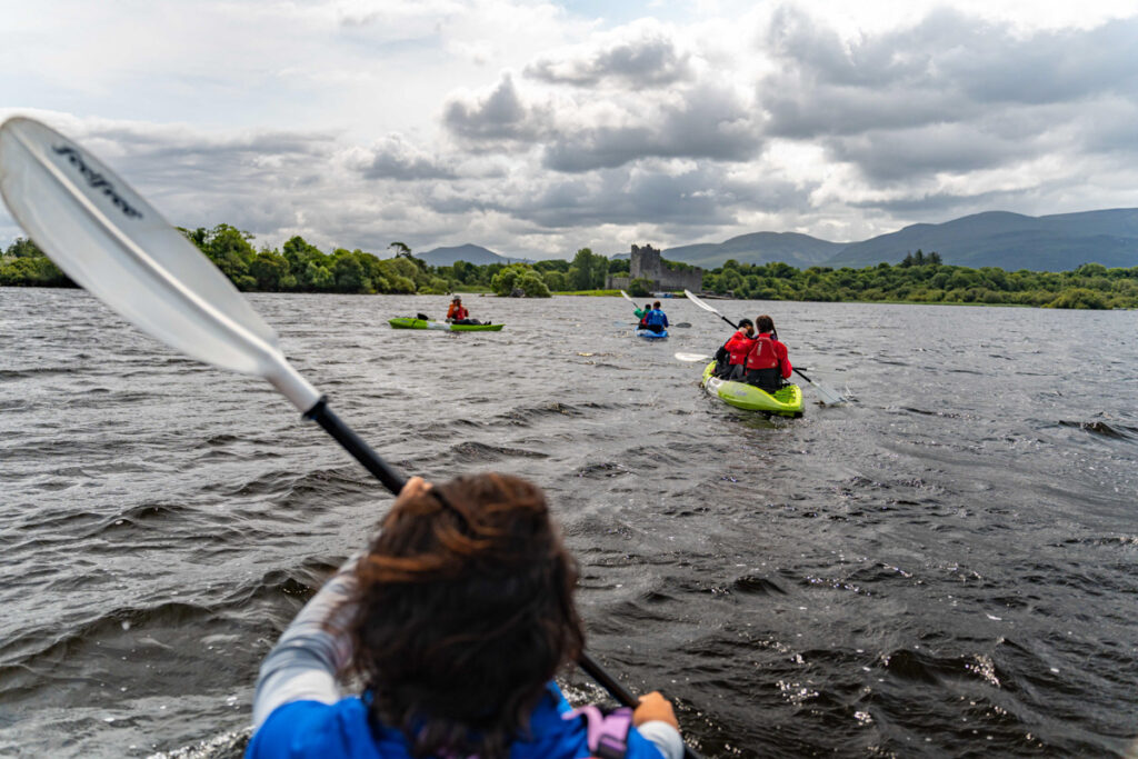 Landscape photo of people during lake kayaking tour. In the background is Ross Castle. Killarney