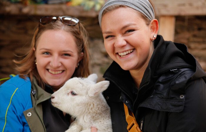 Two women smiling, holding a new born lamb in Ireland