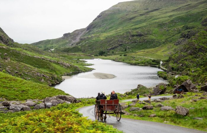 People riding a horse and carriage (jaunting car) through the green hills of Ireland. Photo: Andre Ouellet
