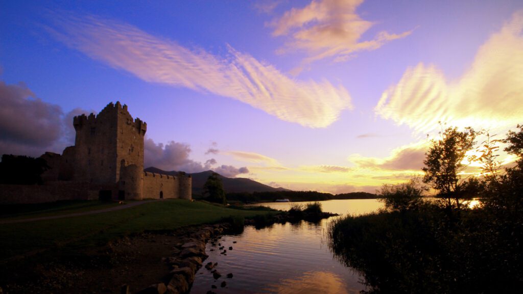 Majestic Ross Castle by the tranquil Lough Leane bathed in the warm glow of a sunset.